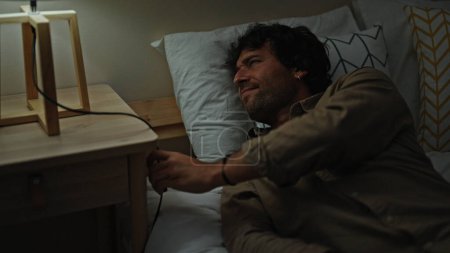Foto de Joven hispano acostado en la cama cansado apagando la luz para dormir en el dormitorio - Imagen libre de derechos