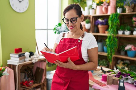 Photo for Young beautiful hispanic woman florist smiling confident writing on notebook at flower shop - Royalty Free Image