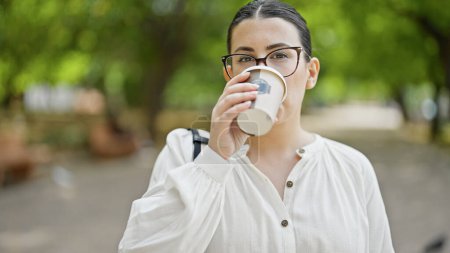 Photo for Young beautiful hispanic woman drinking take away coffee at the park - Royalty Free Image