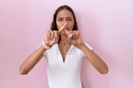 Téléchargez les photos : Jeune femme hispanique portant casual blanc t-shirt rejet expression croisement doigts faire signe négatif - en image libre de droit