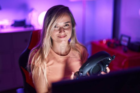 Téléchargez les photos : Jeune femme blonde streamer souriant confiant assis sur la table à la salle de jeux - en image libre de droit