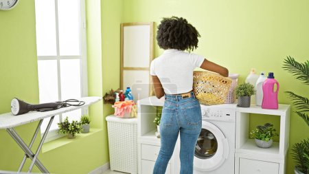 Photo for African american woman holding basket with clothes standing backwards at laundry room - Royalty Free Image