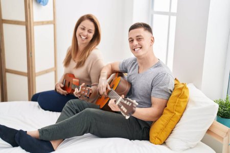 Téléchargez les photos : Man and woman mother and son playing classical guitar and ukulele at bedroom - en image libre de droit