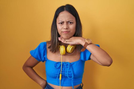Téléchargez les photos : Jeune femme hispanique debout sur fond jaune couper la gorge avec la main comme couteau, menacer d'agression avec une violence furieuse - en image libre de droit