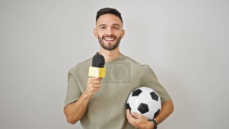 Téléchargez les photos : Jeune homme hispanique journaliste de football travaillant à l'aide d'un microphone tenant ballon de football sur fond blanc isolé - en image libre de droit
