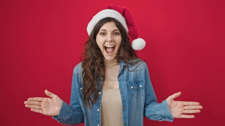 Photo for Young beautiful hispanic woman surprise expression wearing christmas hat over isolated red background - Royalty Free Image