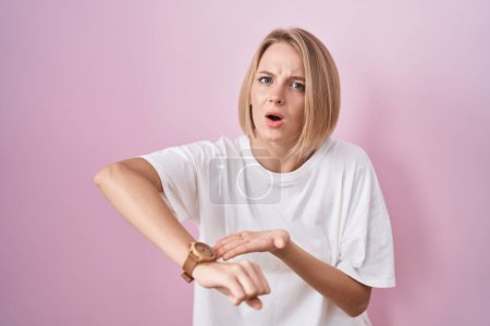 Photo for Young caucasian woman standing over pink background in hurry pointing to watch time, impatience, upset and angry for deadline delay - Royalty Free Image