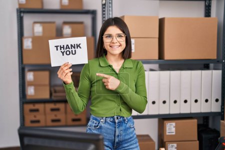 Photo for Young hispanic doctor woman working at small business ecommerce holding thank you banner smiling happy pointing with hand and finger - Royalty Free Image