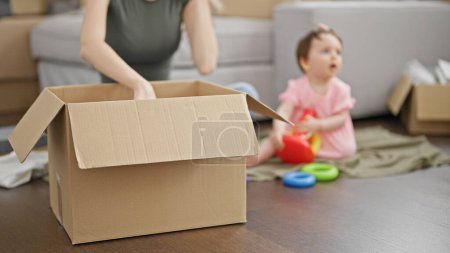 Photo for Mother and daughter packing cardboard box playing on floor at new home - Royalty Free Image