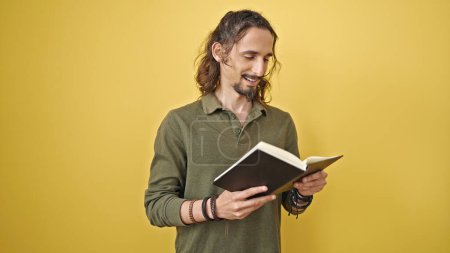 Téléchargez les photos : Jeune homme hispanique lisant un livre souriant sur fond jaune isolé - en image libre de droit