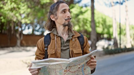 Téléchargez les photos : Jeune homme hispanique touriste portant un sac à dos regardant la carte de la ville au parc - en image libre de droit