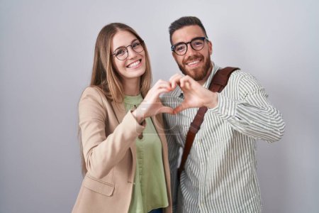 Téléchargez les photos : Jeune couple debout sur fond blanc souriant en amour faisant forme de symbole de coeur avec les mains. concept romantique. - en image libre de droit