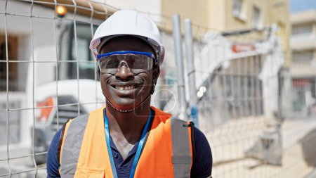 Foto de Hombre afroamericano constructor sonriendo confiado de pie en el lugar de construcción - Imagen libre de derechos