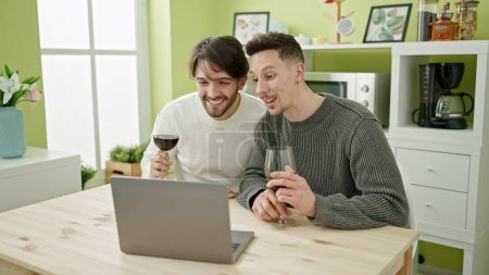 Foto de Dos hombres pareja teniendo videollamada bebiendo copa de vino en el comedor - Imagen libre de derechos