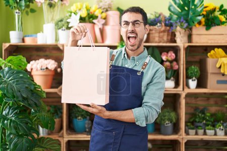 Foto de Hombre hispano guapo trabajando en floristería enojado y loco gritando frustrado y furioso, gritando con ira mirando hacia arriba. - Imagen libre de derechos