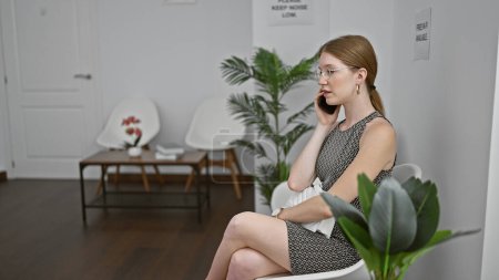 Téléchargez les photos : Jeune femme blonde assise sur une chaise parlant sur smartphone dans la salle d'attente - en image libre de droit
