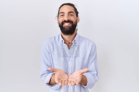 Téléchargez les photos : Homme hispanique à la barbe portant une chemise décontractée souriant avec les mains paumes ensemble recevant ou donnant geste. maintien et protection - en image libre de droit