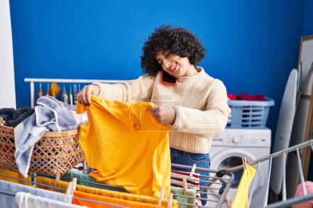 Téléchargez les photos : Young middle east woman talking on the smartphone hanging clothes on clothesline at laundry - en image libre de droit