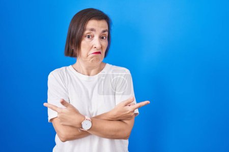 Photo for Middle age hispanic woman standing over blue background pointing to both sides with fingers, different direction disagree - Royalty Free Image