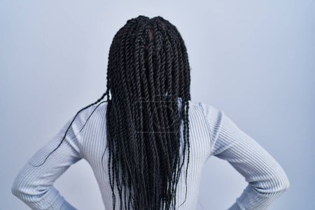 Foto de Mujer afroamericana de pie sobre fondo azul de pie hacia atrás mirando hacia otro lado con los brazos en el cuerpo - Imagen libre de derechos