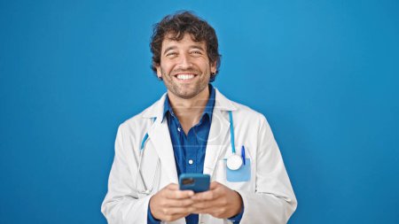 Photo for Young hispanic man doctor using smartphone smiling over isolated blue background - Royalty Free Image
