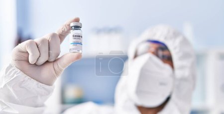 Photo for Young hispanic man scientist wearing medical mask holding covid vaccine dose at laboratory - Royalty Free Image