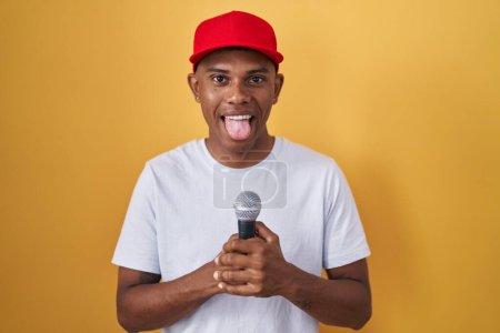Téléchargez les photos : Jeune homme hispanique chantant chanson en utilisant microphone langue collante heureux avec expression drôle. - en image libre de droit