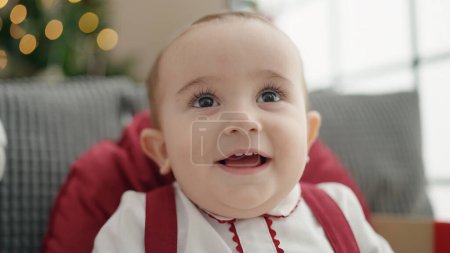 Photo for Adorable hispanic baby smiling confident sitting on sofa by christmas tree at home - Royalty Free Image