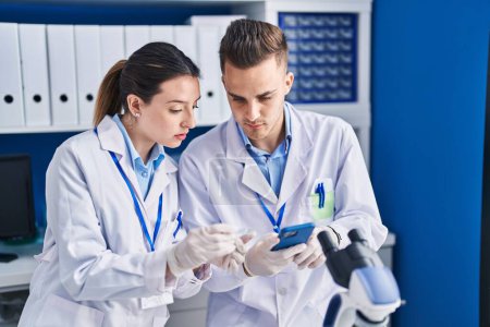 Téléchargez les photos : Man and woman scientists using smartphone looking sample at laboratory - en image libre de droit