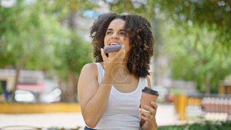 Photo for Young beautiful hispanic woman sending voice message by smartphone drinking coffee at park - Royalty Free Image