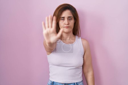 Photo for Brunette woman standing over pink background doing stop sing with palm of the hand. warning expression with negative and serious gesture on the face. - Royalty Free Image