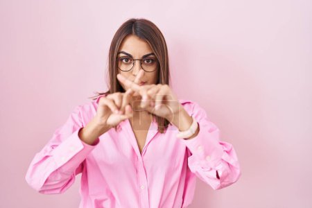 Téléchargez les photos : Jeune femme hispanique portant des lunettes debout sur fond rose expression de rejet en croisant les doigts faisant signe négatif - en image libre de droit