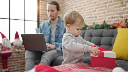 Foto de Padre e hijo desempaquetando el regalo de Navidad usando el ordenador portátil en casa - Imagen libre de derechos