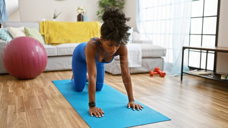 Photo for African american woman wearing sportswear stretching back at home - Royalty Free Image