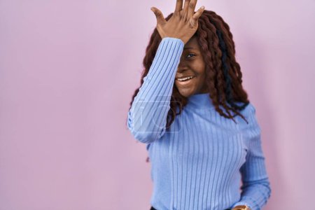 Téléchargez les photos : Femme africaine debout sur fond rose surpris avec la main sur la tête pour erreur, rappelez-vous erreur. oublié, mauvais concept de mémoire. - en image libre de droit