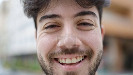Téléchargez les photos : Jeune homme hispanique souriant confiant debout dans la rue - en image libre de droit