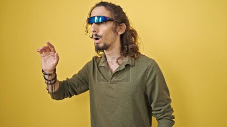 Foto de Joven hispano jugando videojuegos con gafas de realidad virtual sobre fondo amarillo aislado - Imagen libre de derechos