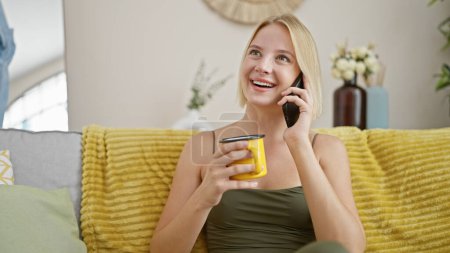 Téléchargez les photos : Young blonde woman talking on smartphone drinking coffee at home - en image libre de droit