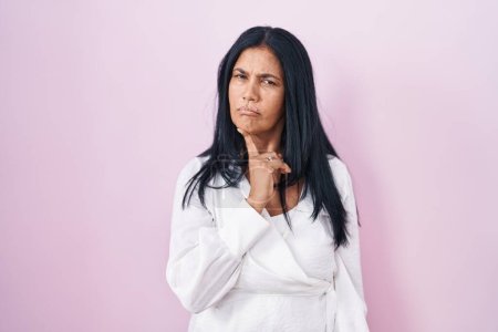 Photo for Mature hispanic woman standing over pink background thinking concentrated about doubt with finger on chin and looking up wondering - Royalty Free Image