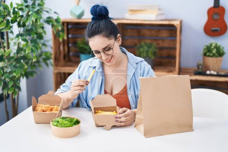 Photo for Young caucasian woman eating take away food sitting on table at home - Royalty Free Image