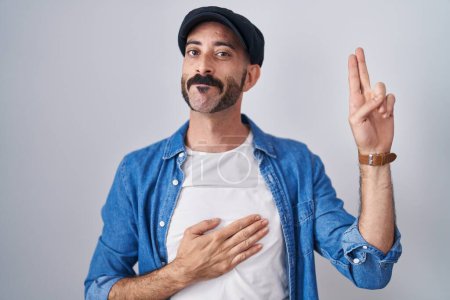 Photo for Hispanic man with beard standing over isolated background smiling swearing with hand on chest and fingers up, making a loyalty promise oath - Royalty Free Image