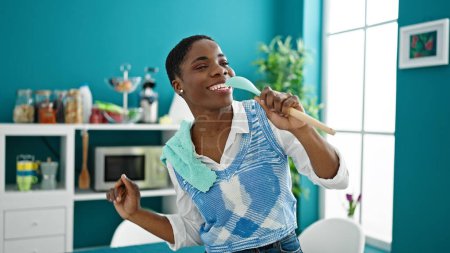 Foto de Mujer afroamericana cantando canción usando cuchara como micrófono en el comedor - Imagen libre de derechos