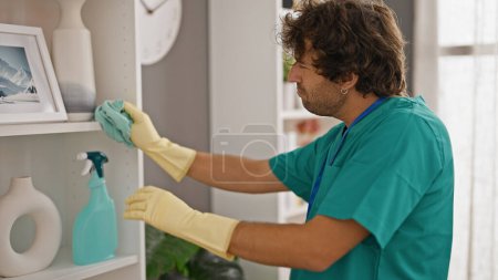 Foto de Joven hombre hispano limpiando estanterías con un paño en casa - Imagen libre de derechos