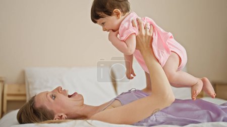 Téléchargez les photos : Mère et fille couchées sur le lit tenant bébé en l'air dans la chambre - en image libre de droit