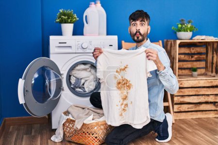 Photo for Young hispanic man with beard holding clean white t shirt and t shirt with dirty stain making fish face with mouth and squinting eyes, crazy and comical. - Royalty Free Image