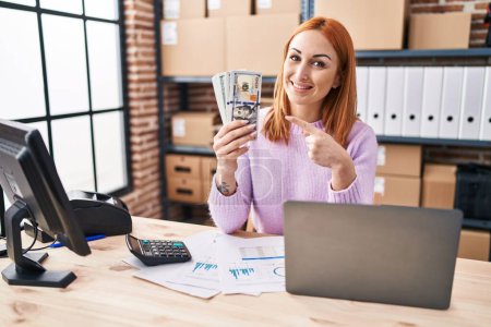Téléchargez les photos : Jeune femme travaillant dans une petite entreprise e-commerce tenant de l'argent souriant heureux pointant avec la main et le doigt - en image libre de droit