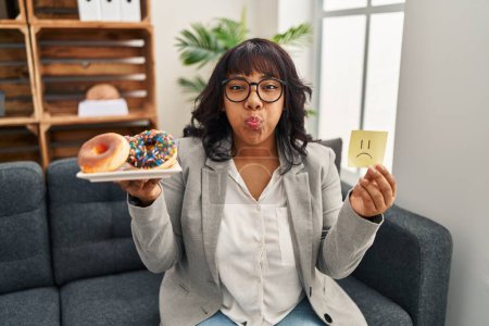 Photo for Hispanic therapist woman working on eating disorder puffing cheeks with funny face. mouth inflated with air, catching air. - Royalty Free Image