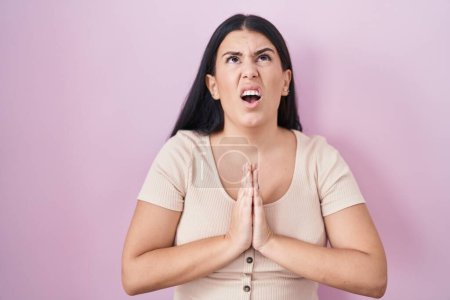 Photo for Young hispanic woman standing over pink background begging and praying with hands together with hope expression on face very emotional and worried. begging. - Royalty Free Image