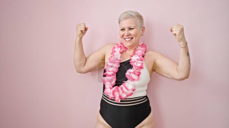 Téléchargez les photos : Femme aux cheveux gris du Moyen Âge portant un maillot de bain et un lei hawaïen avec un geste gagnant sur un fond rose isolé - en image libre de droit