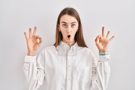 Photo for Young caucasian woman standing over isolated background looking surprised and shocked doing ok approval symbol with fingers. crazy expression - Royalty Free Image